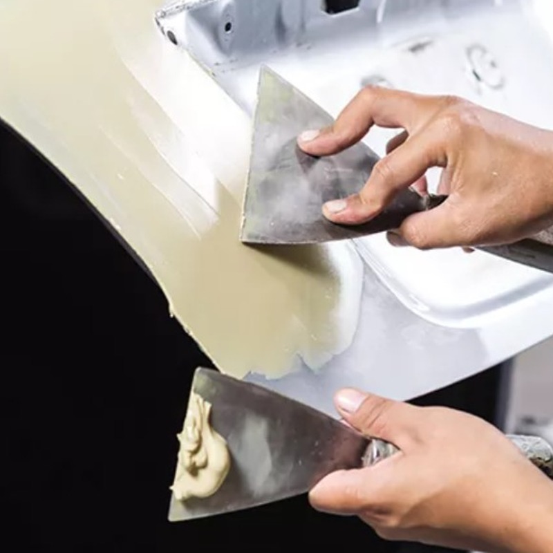 Applying flexible putty resin with putty knives on auto body panel